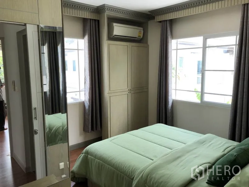 Detached House for rent or sale in Bang Kapi, Bangkok - Cozy bedroom with built-in wardrobe, air conditioner and double bed by corner windows.