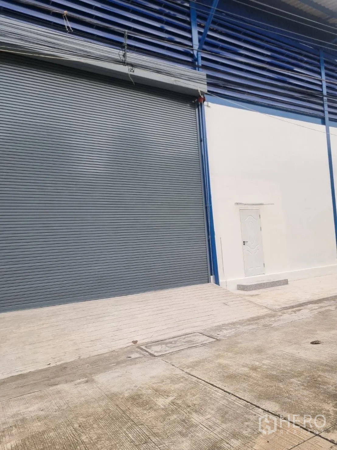 Warehouse for rent in Thepharak, Nakhon Ratchasima - Exterior view with a large roller shutter door and side personnel door.