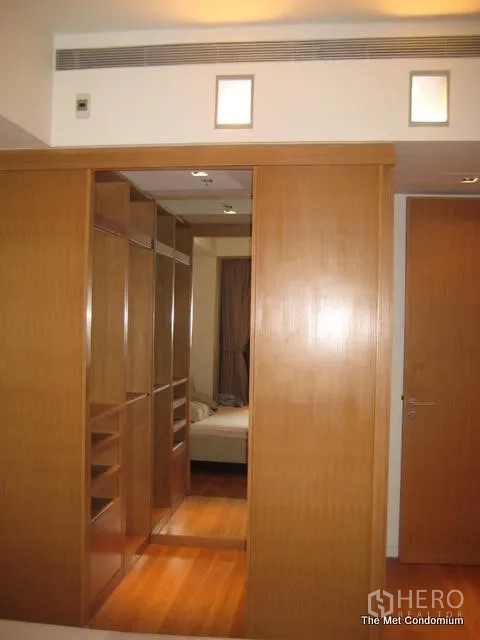 Condominium for rent or sale in Sathon, Bangkok - Walk-in closet with custom wood cabinetry leading toward the bedroom in a two-bedroom unit.