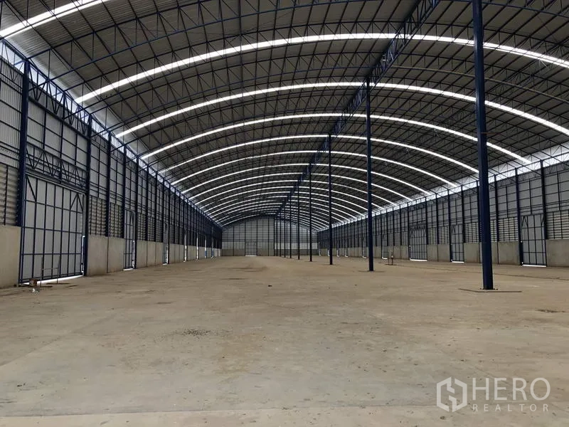 Factory for rent or sale in Lat Lum Kaeo, Pathum Thani - Expansive warehouse interior with arched steel trusses and daylight strips along the roof.