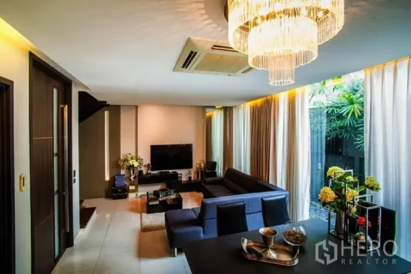 ทาวน์เฮาส์ ให้เช่าหรือขายในWatthana, Bangkok - ห้องนั่งเล่นแบบเปิดโล่ง โซฟารูปตัวแอล โคมระย้า และกระจกเต็มบานมองสวนน้อย