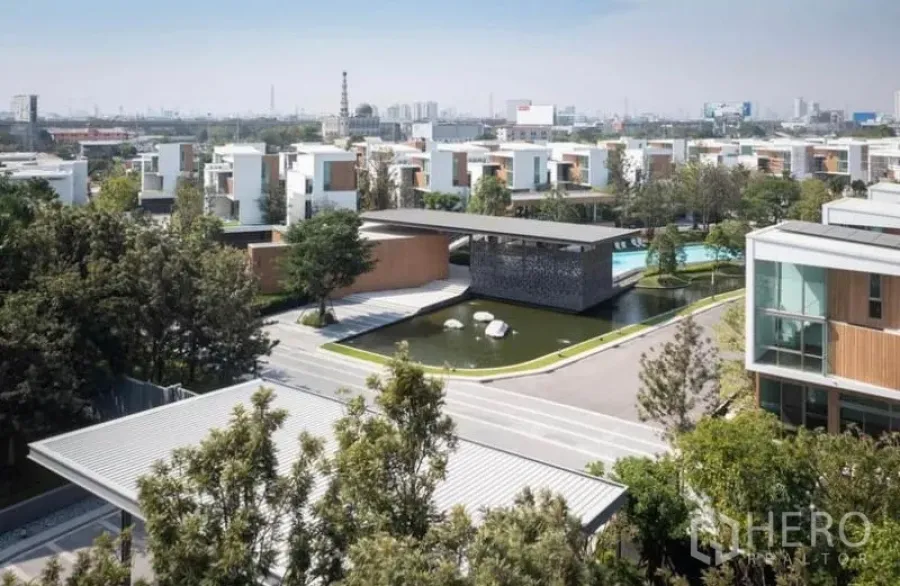 Detached House for rent in Saphan Sung, Bangkok - Aerial view of a modern gated community featuring a pond, clubhouse and white detached houses