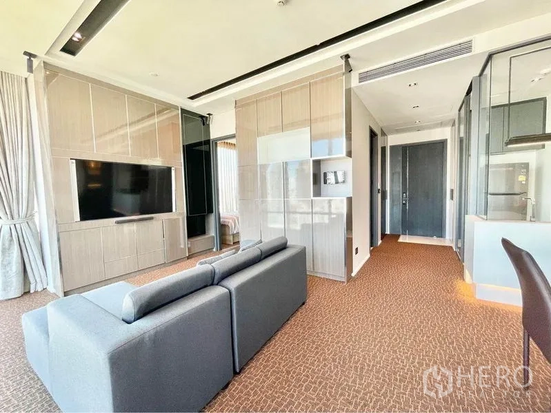 Condominium for rent in Watthana, Bangkok - Living room with large TV on built-in wall cabinetry and corridor leading to bedrooms.