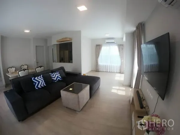 Detached House for rent in Prawet, Bangkok - Bright open-plan living room with large L-shaped sofa, wall-mounted TV and full-height windows.