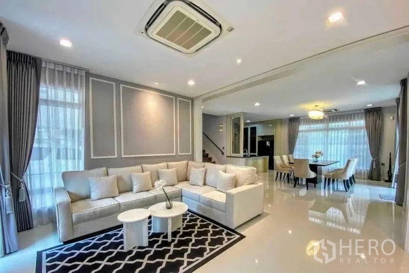 Detached House for rent in Bang Khen, Bangkok - Open-plan living and dining room with L-shaped sofa and floor-to-ceiling windows.