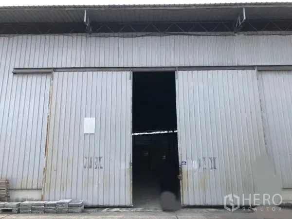 货栈 出租在Pak Kret, Nonthaburi - 仓库正面，部分开启的滑动门与混凝土前场。