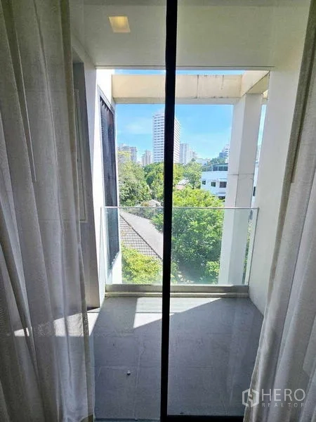 Condominium for rent - Small balcony with glass railing overlooking trees and city skyline.