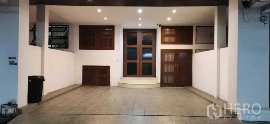 Townhouse for rent in Khlong Toei, Bangkok - Covered carport with tiled floor, recessed lighting, and wood‑framed doors.