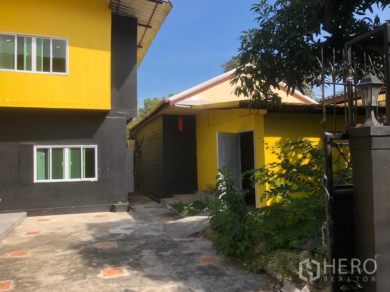 บ้าน ให้เช่าในKhlong Toei, Bangkok - ลานกว้างคั่นระหว่างตัวบ้านหลักกับอาคารเล็กสีเหลือง มีหน้าต่างบานเลื่อนและต้นไม้ริมทางเดิน