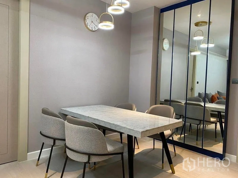 公寓 出售在Huai Khwang, Bangkok - 餐区特写，大理石桌面、灰色软椅和通高镜面墙，环形吊灯点缀。