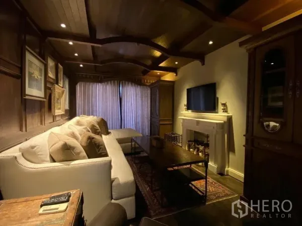 Condominium for rent in Khlong San, Bangkok - Cozy media room with wood‑paneled ceiling, large sectional sofa and decorative fireplace.