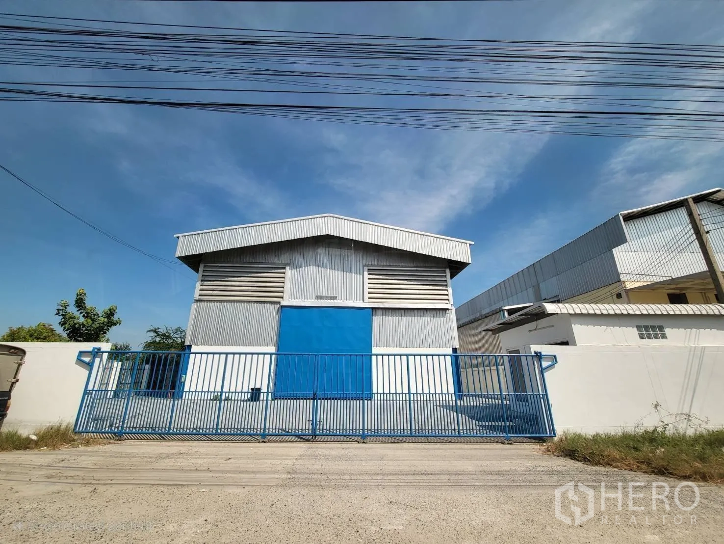 Warehouse for rent in Mueang Samut Prakan, Samut Prakan - Street-side perspective showing the secure fence and main warehouse entrance.