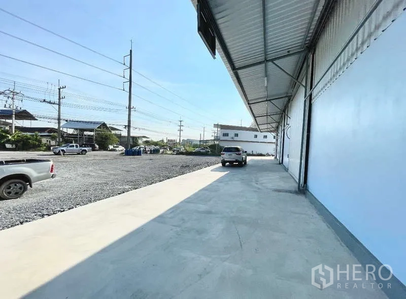 货栈 出租在Krathum Baen, Samut Sakhon - 仓库前方的装卸雨棚与宽混凝土车道，可见周边道路与建筑。