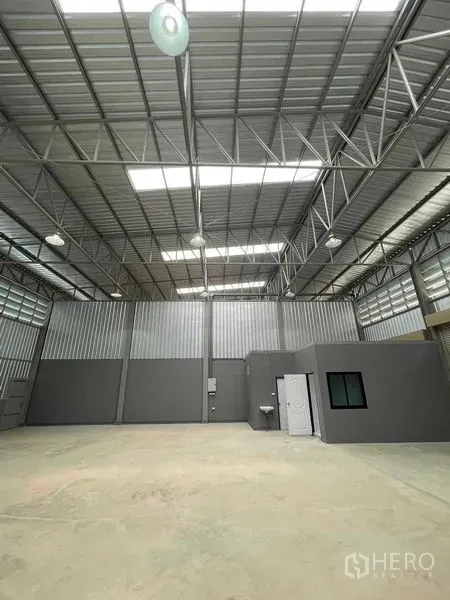 Warehouse for rent in Phra Samut Chedi, Samut Prakan - Warehouse interior with a built‑in office and restroom, metal sheet walls, bright lights, and polished concrete floor.