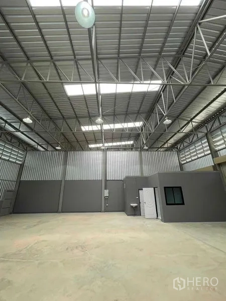 Warehouse for rent in Phra Samut Chedi, Samut Prakan - Warehouse interior with a built‑in office and restroom, metal sheet walls, bright lights, and polished concrete floor.