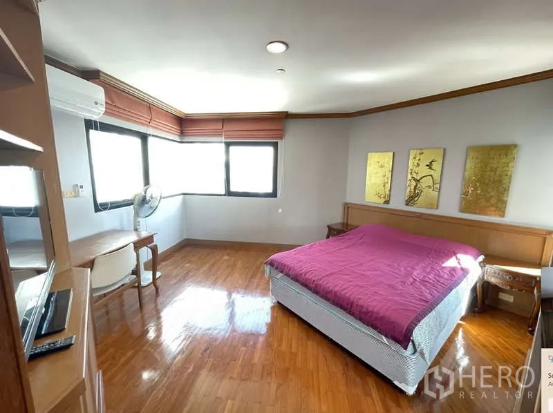 คอนโด ให้เช่า - ห้องนอนมุมพร้อมหน้าต่างหลายด้าน โต๊ะทำงาน และเตียงผ้าคลุมสีม่วง