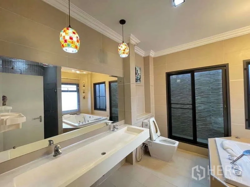 独立式住宅 出租在Mueang Nonthaburi, Nonthaburi - 宽敞卫浴配超长双台盆、大镜面、彩色吊灯与坐便器。