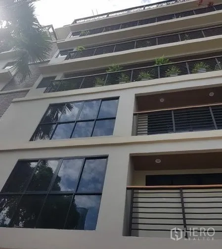 Apartment for rent in Khlong Toei, Bangkok - Modern mid-rise apartment facade with large windows and metal balcony railings.