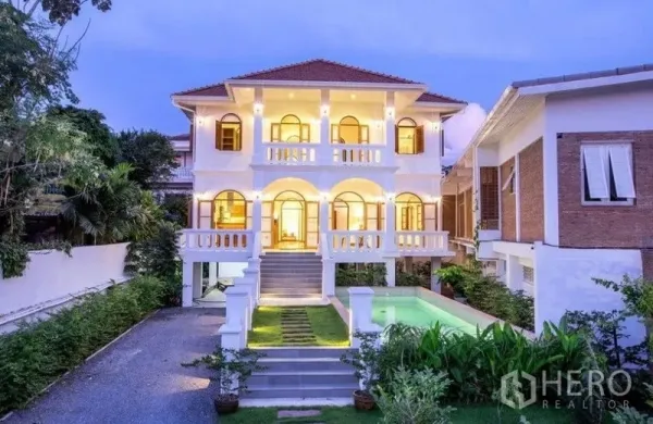 独立式住宅 出租在Phra Khanong, Bangkok - 三层独栋外立面，拱窗与阳台，花园和泳池在暮色中