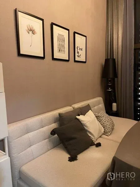 คอนโด ให้เช่าในRatchathewi, Bangkok - โซฟาพร้อมหมอนอิงและกรอบรูปบนผนัง ข้างผ้าม่านทิ้งยาวในห้องนั่งเล่น