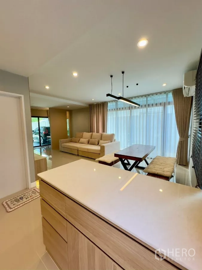 独立式住宅 出租在Samut Prakan - 从厨房岛台望向明亮的客餐厅，纱帘通透明亮。