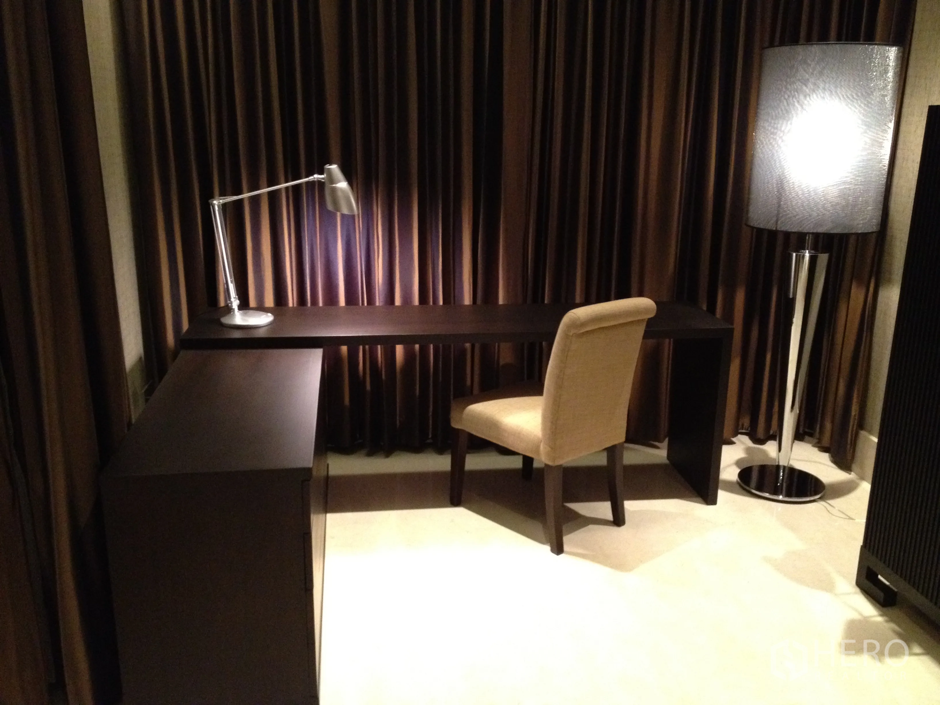 Condominium for rent in Bang Rak, Bangkok - L-shaped dark wood study desk with task lamp and beige chair beside a floor lamp and full drapes.