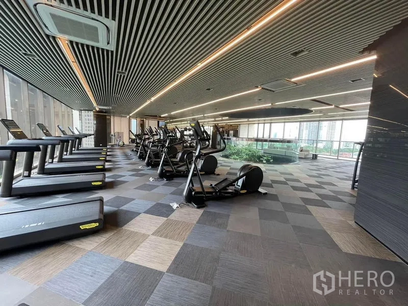 Condominium for rent in Samut Prakan - Large fitness center with treadmills and bikes facing wide windows.