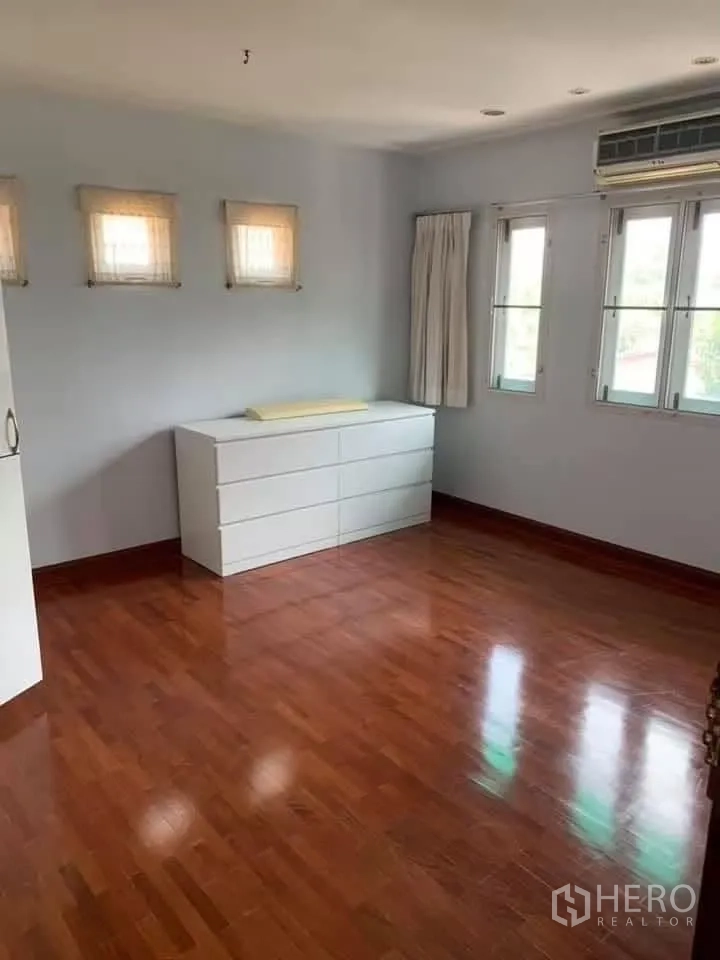 Townhouse for rent in Watthana, Bangkok - Bright bedroom with wood flooring, air conditioner, windows, and white dresser.