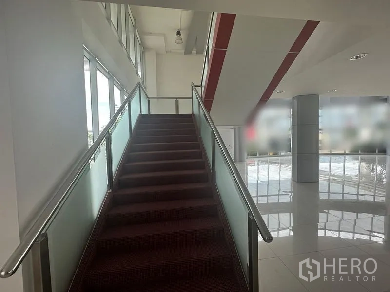 Retail Space for rent in Prawet, Bangkok - Wide staircase with glass balustrade leading to the mezzanine in a contemporary showroom.