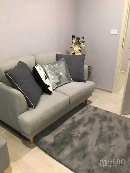 คอนโด ขายในBang Na, Bangkok - โซฟาสองที่นั่งสีเทาพร้อมพรมขนนุ่มและหมอนอิงในห้องนั่งเล่นที่เป็นระเบียบ