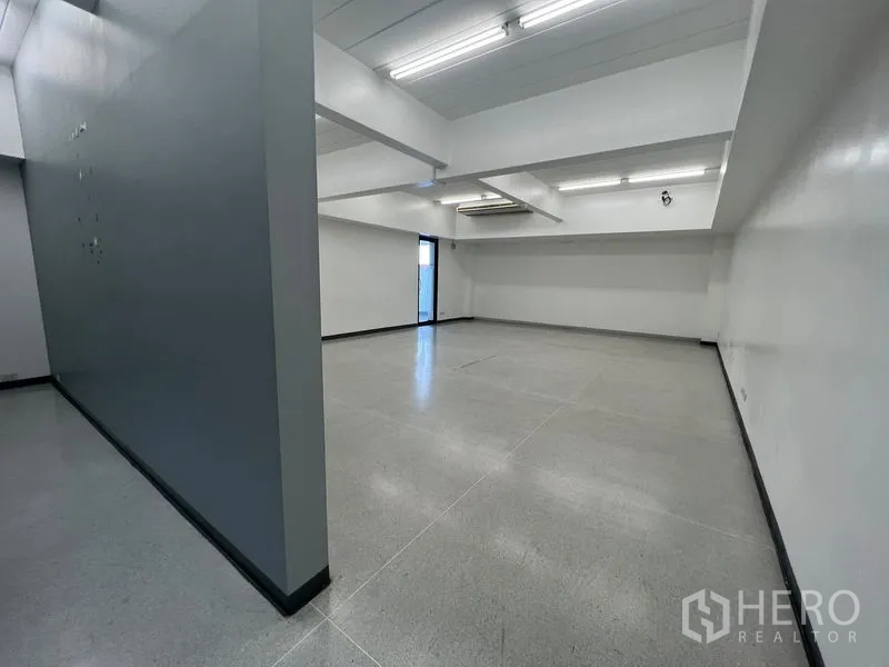 Office Space for rent in Mueang Samut Prakan, Samut Prakan - Open-plan room with a gray feature wall, ceiling lights, and an exit door.