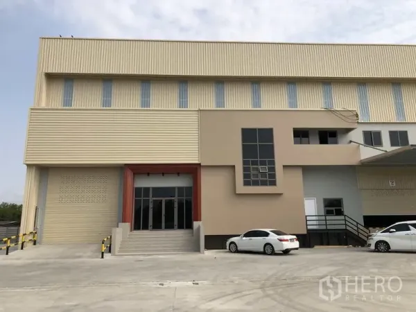 工厂 出租或出售在Samut Prakan - 工厂正立面，带办公楼、玻璃入口及停车区域。