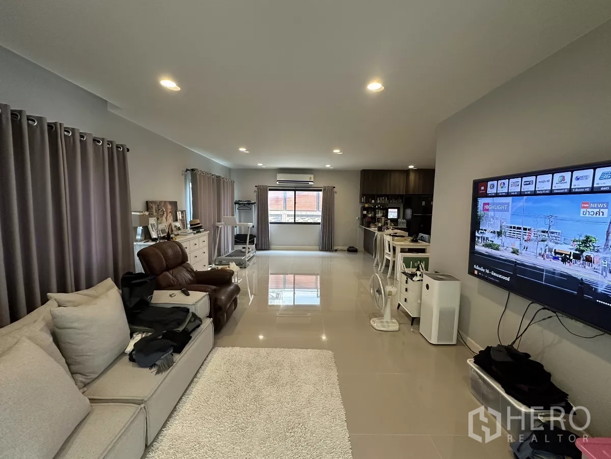 บ้าน ให้เช่าหรือขายในLam Luk Ka, Pathum Thani - ห้องนั่งเล่นแบบโอเพ่นสเปซ กว้างขวาง โซฟา ทีวีติดผนัง ไฟดาวน์ไลท์ และพื้นกระเบื้องเงา