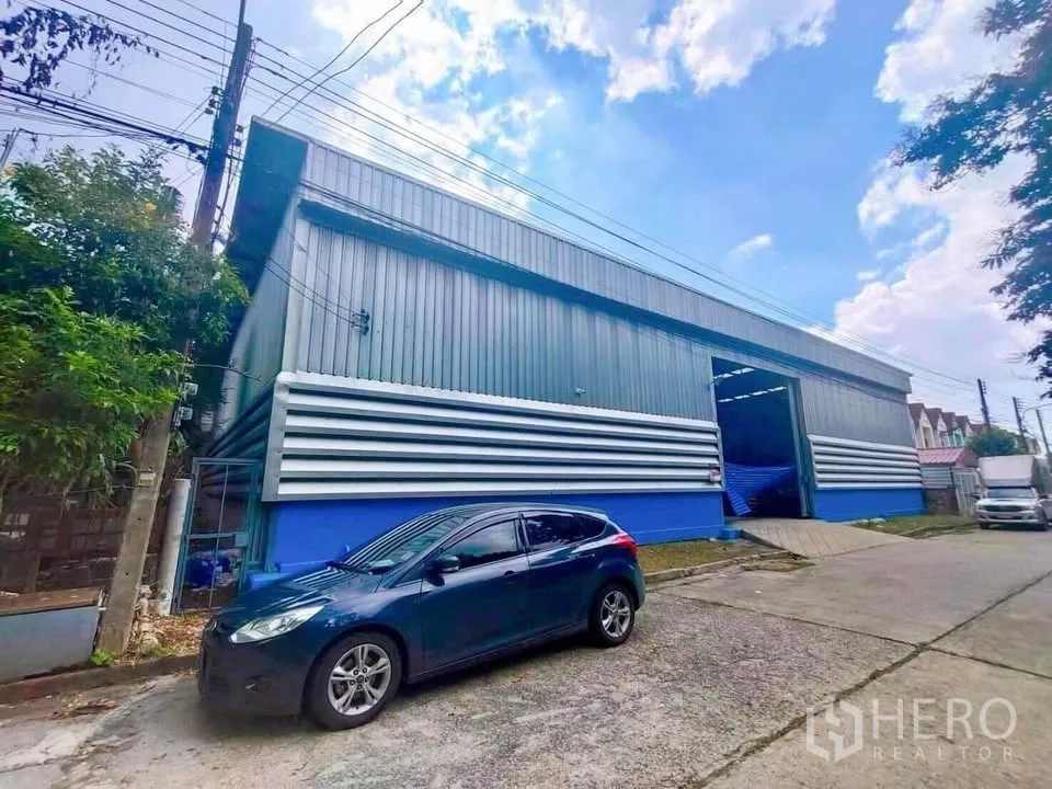 คลังสินค้า ให้เช่าในThanyaburi, Pathum Thani - ด้านหน้าโกดังพร้อมประตูขนถ่าย เปิดโล่ง ฐานสีน้ำเงิน และทางรถเข้าออกสะดวก