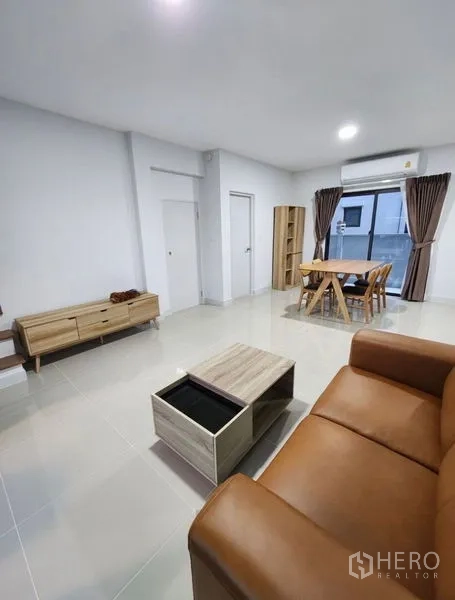 Townhouse for rent in Bang Phli, Samut Prakan - Spacious living room with sofa, coffee table, dining set, and sliding glass doors with curtains.