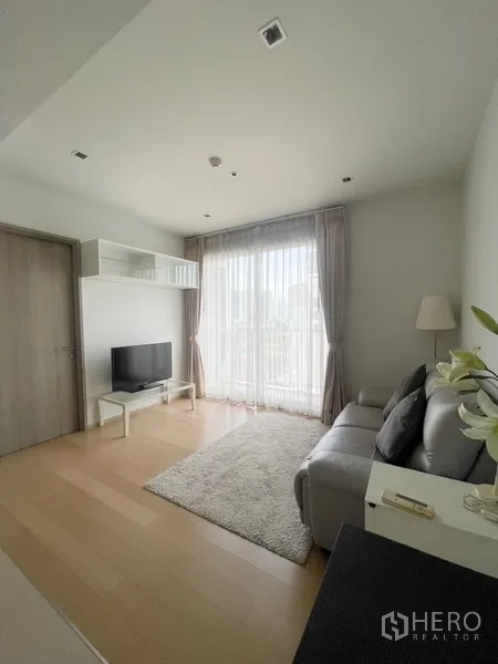 Condominium for rent in Watthana, Bangkok - Cozy living area with TV console, large window and sheer curtains bringing natural light.