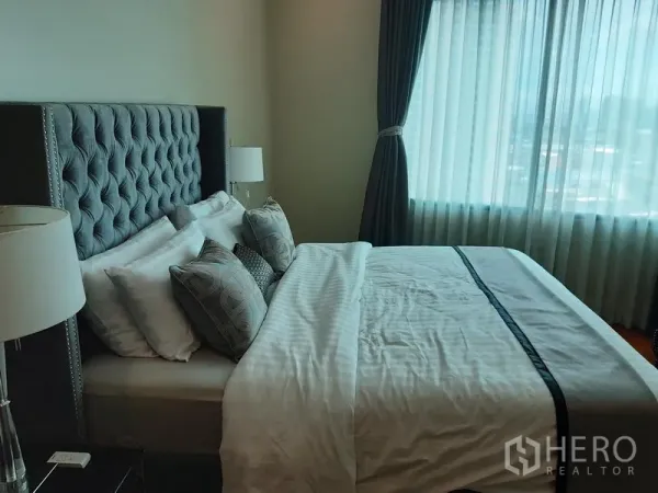 คอนโด ให้เช่าหรือขายในKhlong Toei, Bangkok - ห้องนอนใหญ่ เตียงหัวบุผ้าทัฟต์ โคมข้างเตียง และหน้าต่างบานกว้างพร้อมผ้าม่าน