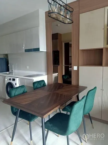 Condominium for rent in Pathum Wan, Bangkok - Dining area with wooden table and green chairs beside the open kitchen cabinetry.
