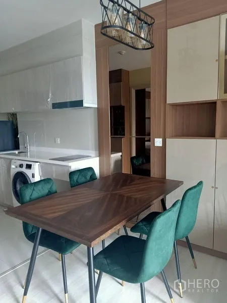 Condominium for rent in Pathum Wan, Bangkok - Dining area with wooden table and green chairs beside the open kitchen cabinetry.