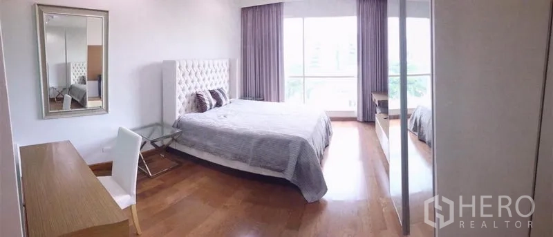 คอนโด ให้เช่าในPathum Wan, Bangkok - ห้องนอนกว้าง เตียงคิงไซซ์ หัวเตียงบุผ้า โต๊ะทำงาน ตู้เสื้อผ้าบานกระจก และหน้าต่างใหญ่พร้อมผ้าม่าน