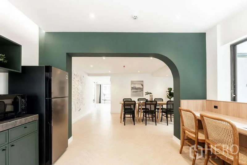 Office Space for rent in Watthana, Bangkok - Kitchenette with archway leading to a shared workspace with dining-style tables and window seating.