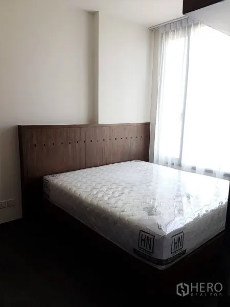 Condominium for rent or sale in Watthana, Bangkok - Cozy bedroom with wooden headboard and a large window bringing in natural light.