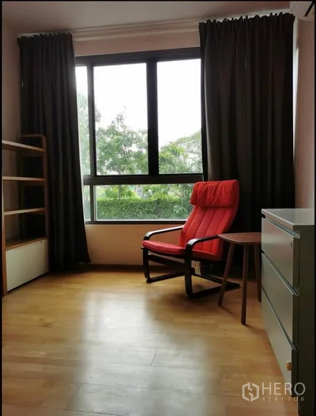 คอนโด ให้เช่าในKhlong Toei, Bangkok - ห้องสว่างพร้อมเก้าอี้เอนสีแดง หน้าต่างบานใหญ่และวิวต้นไม้