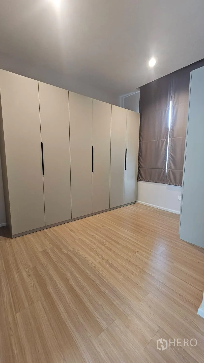 Townhouse for rent in Saphan Sung, Bangkok - Bedroom with full-height wardrobes and wood-look flooring beside a curtained window.