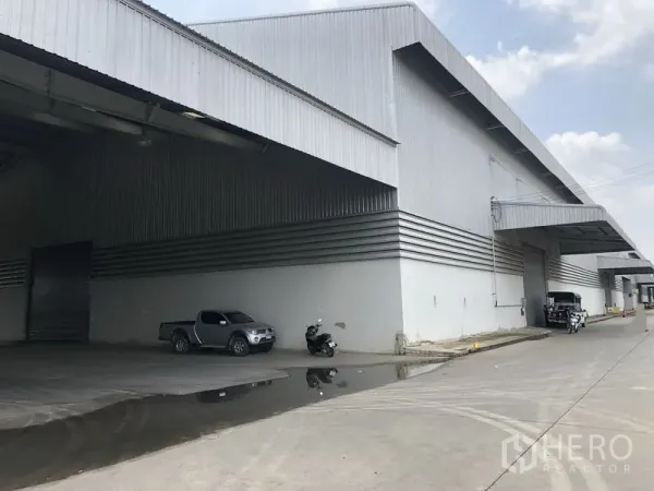 工厂 出租在Wang Noi, Phra Nakhon Si Ayutthaya - 金属外墙仓库外立面，设有大面积雨棚装卸区与卷闸门，前方为混凝土车道。