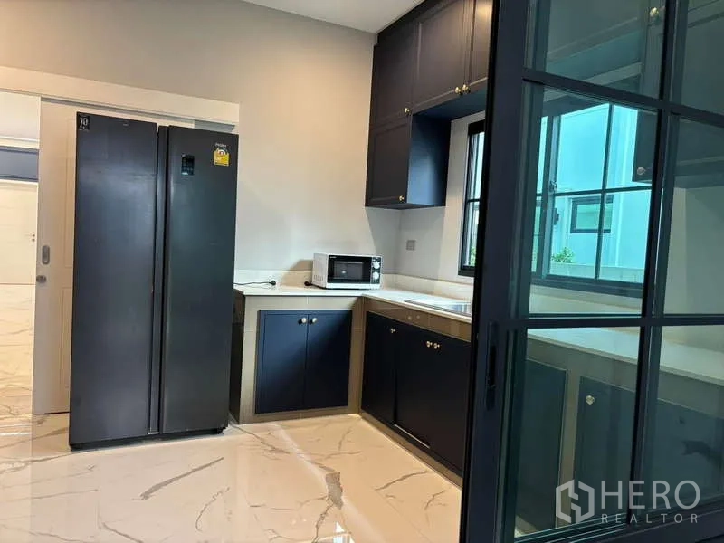 Detached House for rent in Bang Phli, Samut Prakan - Fitted kitchen with navy cabinetry, side-by-side fridge and sliding glass door.
