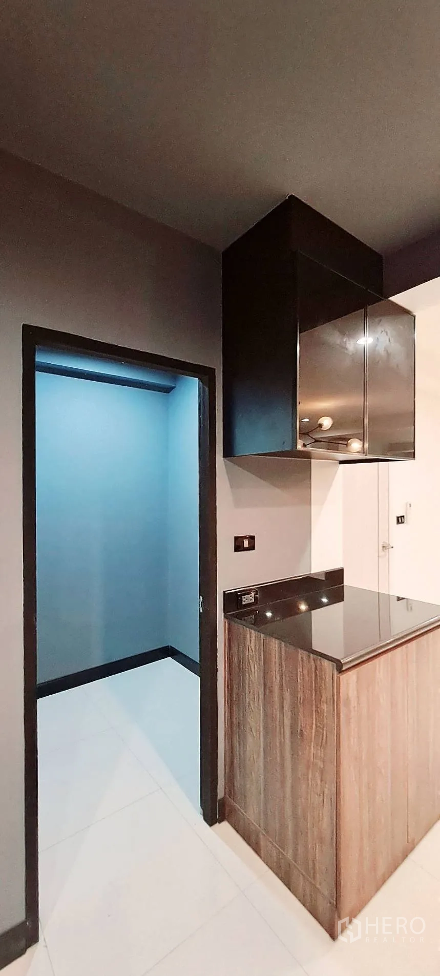Apartment for rent in Phra Khanong, Bangkok - Compact pantry area with black cabinetry beside a doorway to an adjoining room.