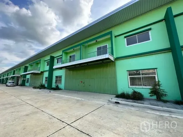 货栈 出租在Pathum Thani - 绿色仓库外观另一角度，宽车道与雨棚一览。