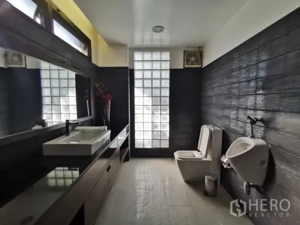 Home Office for sale in Wang Thonglang, Bangkok - Modern restroom with long vanity, square basin, toilet and urinal, lit by a glass-block window.