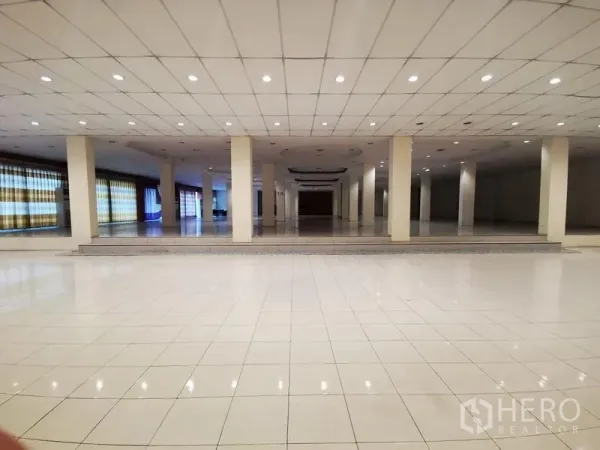 Retail Space for rent in Lam Luk Ka, Pathum Thani - Expansive tiled showroom interior with multiple columns, recessed lights and a raised platform area.